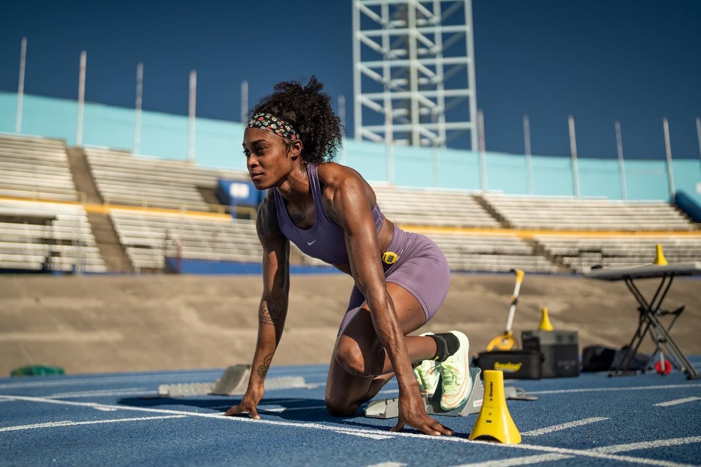 Female sprinter in starting position on a track preparing for a sprint with timing equipment nearby