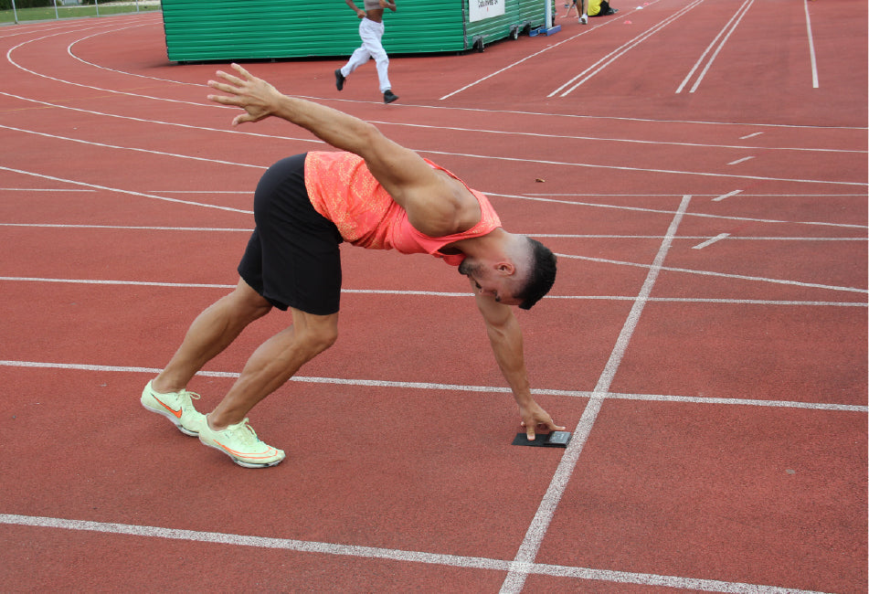 Sprinter in a three-point start position on a track preparing for acceleration training