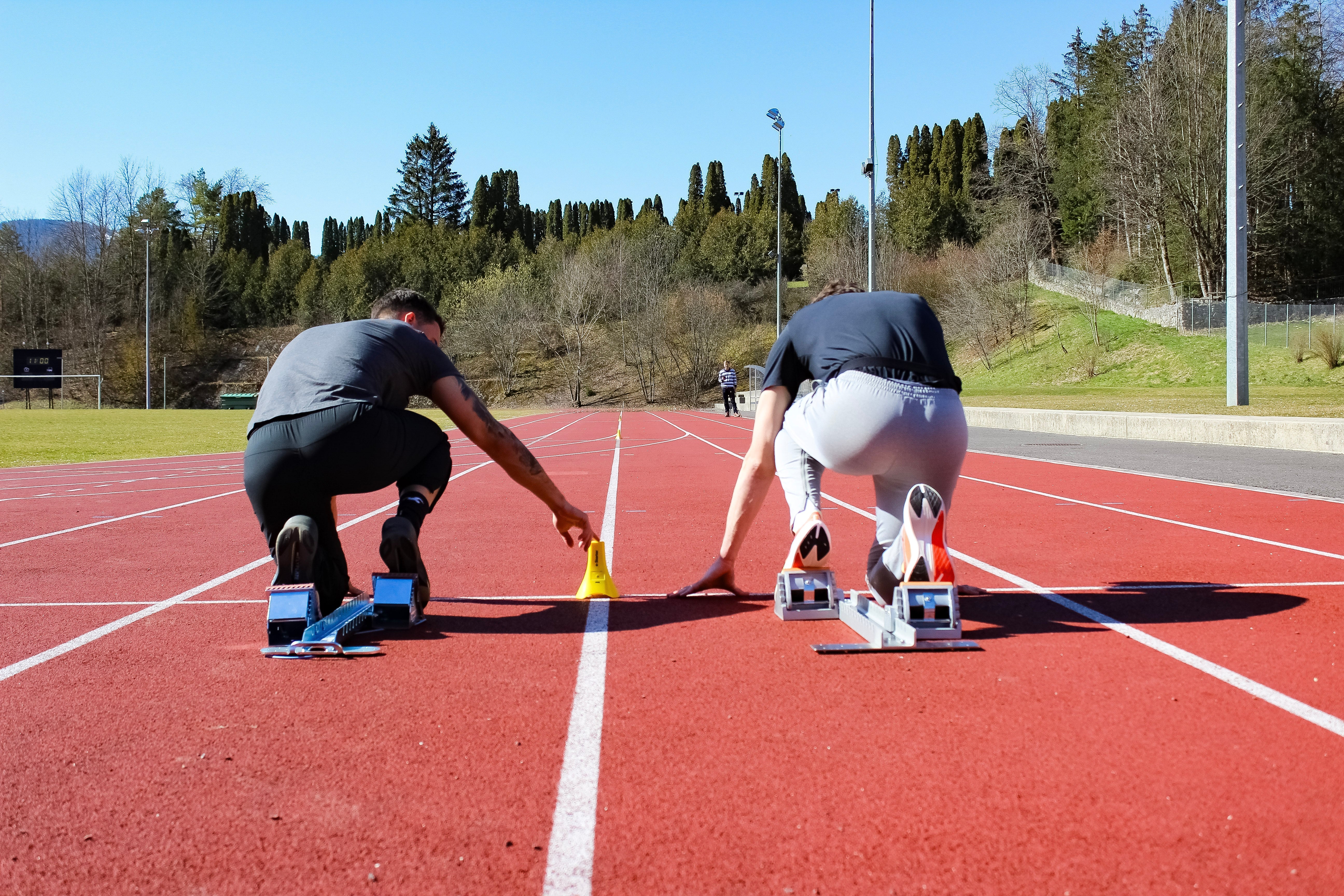 Two sprinters in starting positions on a track preparing for a sprint with timing markers placed between lanes